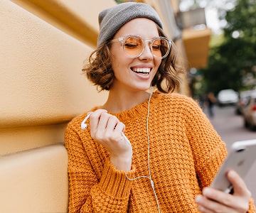 Smiling woman in orange sweater listening to music on phone